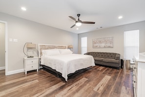 A bedroom with a bed, a nightstand, a dresser, a ceiling fan, and a window with blinds.