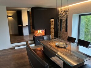 A modern dining area with a glass-top table, black chairs, and a built-in fireplace. - La Vue: 4½-room home in Valposchiavo (Poschiavo)