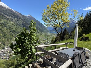 A scenic view of a mountainous area with a dining area featuring a table and chairs. - La Vue: 4½-room home in Valposchiavo (Poschiavo)