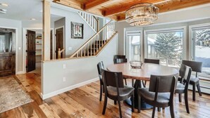 Un comedor espacioso con una mesa y sillas de madera, un candelabro y una escalera que sube a otro nivel.