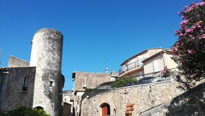Eine schmale Gasse mit Steinhäusern, einem markanten zylindrischen Turm und einem Balkon mit schmiedeeisernem Geländer.