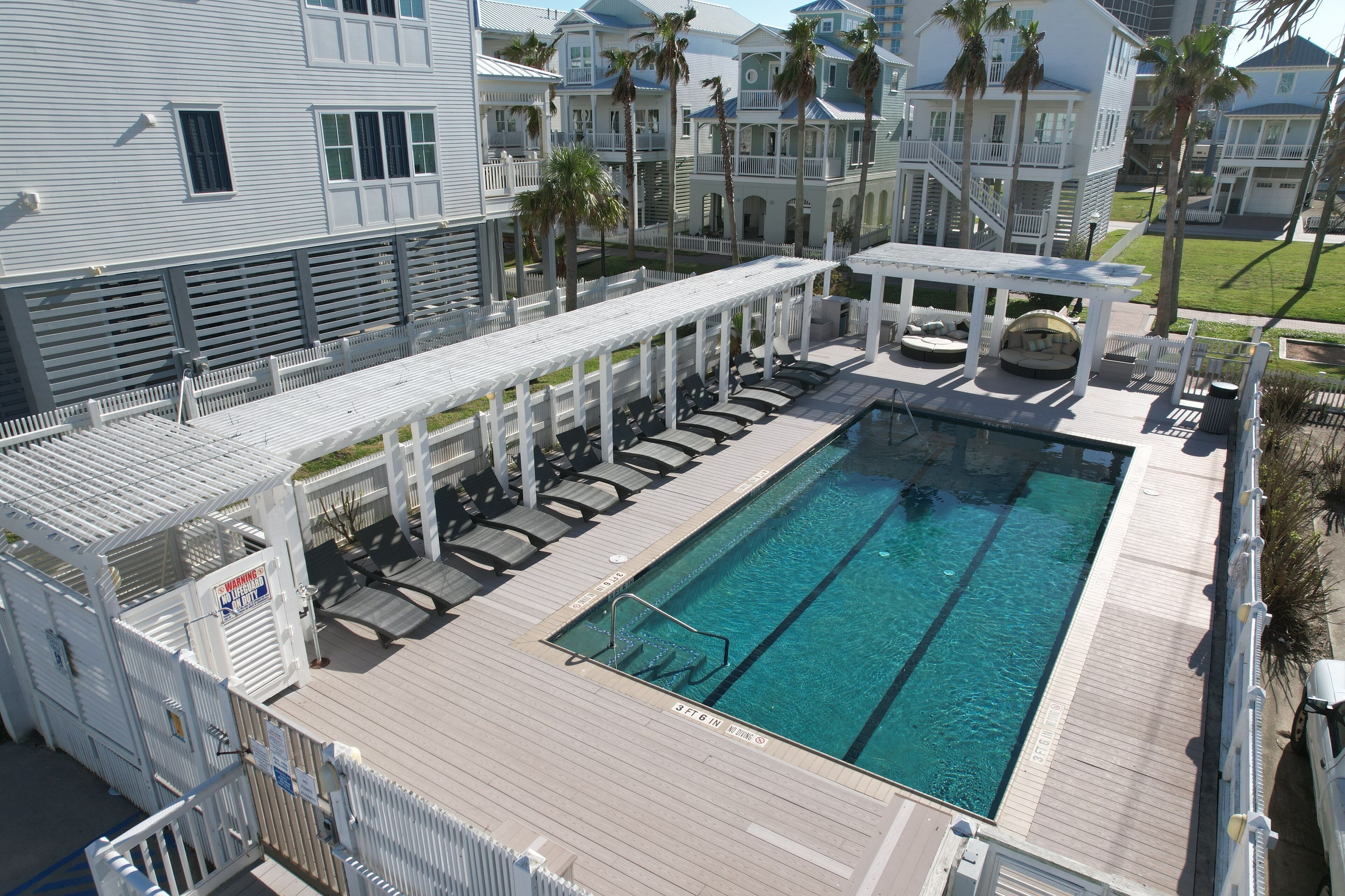 A pool area with a wooden deck, lounge chairs, and a small seating area.