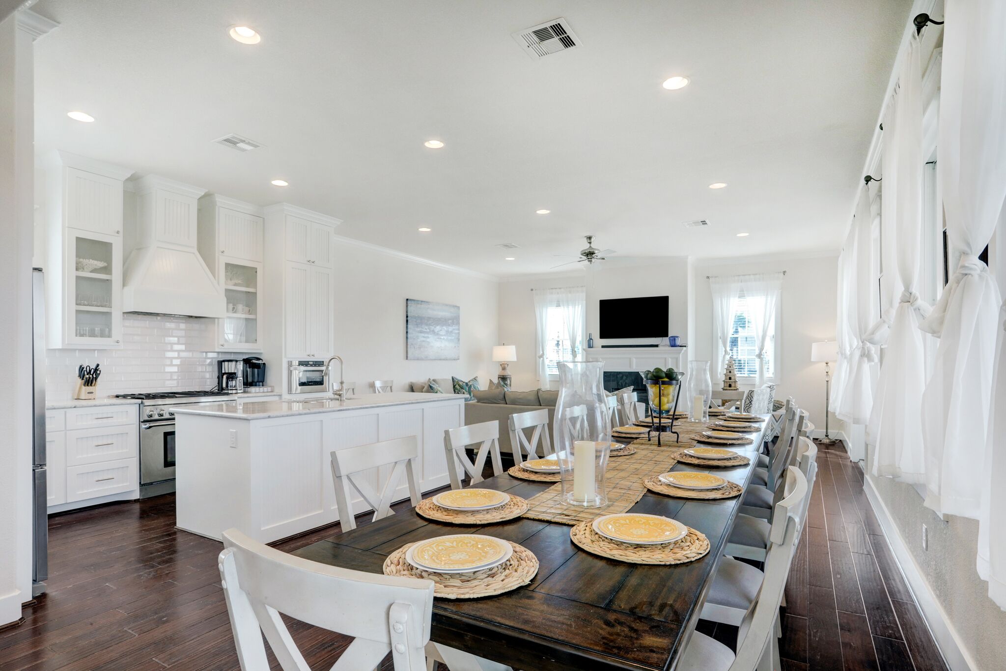 A spacious kitchen with white cabinetry, a central island, and a long dining table set for six.