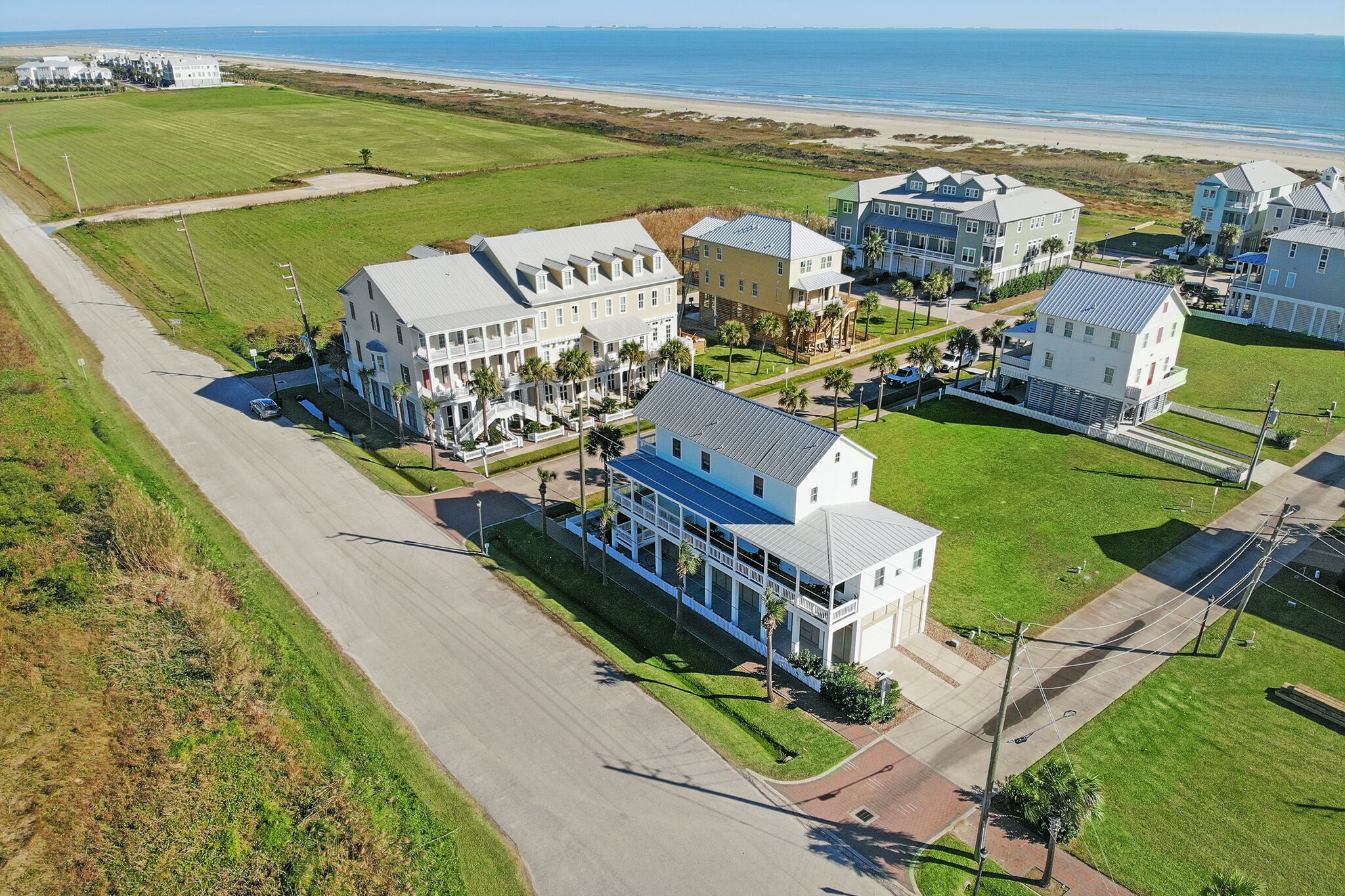 An aerial view of a coastal residential area with houses, a road, and a beach in the background.