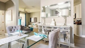 A modern dining area with a glass table, chairs, and a decorative mirror above.