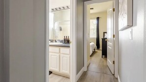 A hallway leading to a bathroom with a vanity, a shower, and a bed in the adjacent room.