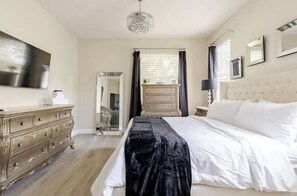 Une chambre à coucher comprenant un lit, une commode, un miroir, un lustre et un téléviseur.