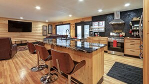 Interior moderno de una cabaña de troncos con cocina, comedor y un televisor grande.