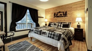 Un dormitorio con cama, dos mesitas de noche, una ventana con cortinas, una lámpara de pared y un cabecero de madera con decoración de silueta de montaña.