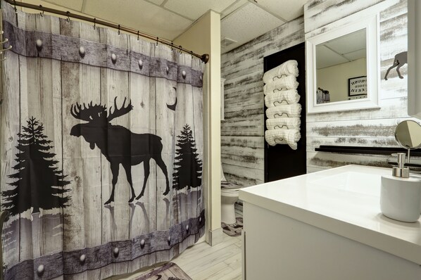 A bathroom with a rustic shower curtain featuring a moose design, a white sink, and a mirror above it. - Alaskan 2300 sq ft Modern Cabin Hotel Like home with Hot Tub (Anchorage)