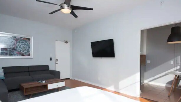 A modern bedroom with a bed, a sofa, a coffee table, a ceiling fan, a TV, and a door leading to another room. - Mid Century Modern Beachside. Laundry. Parking (San Pedro)