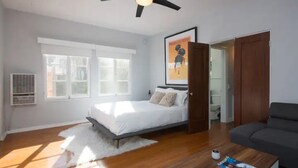 A bedroom with a bed, a ceiling fan, a window, a door, and a small table with a magazine. - Mid Century Modern Beachside. Laundry. Parking (San Pedro)