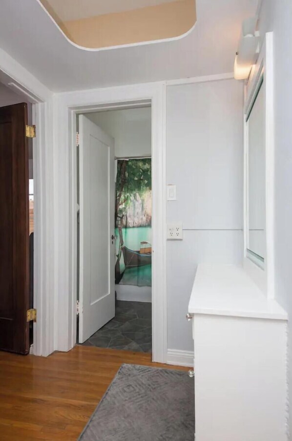 Un couloir doté d’un plancher en bois, de murs blancs et d’une porte donnant sur une pièce où est suspendu un rideau vert.