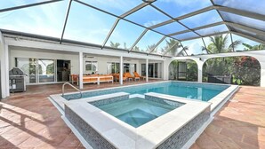 A covered outdoor swimming pool with a patio area, lounge chairs, and a barbecue grill. - Luxurious Naples Home. Heated Pool. Mins to Beach. (Naples)