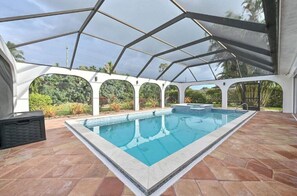 Ein Schwimmbecken mit Glasumrandung, umgeben von einer gefliesten Terrasse und Blick auf Grünflächen.