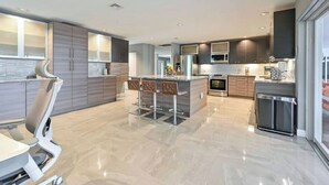 A modern kitchen with a central island, bar stools, and a dining area with a white table and chairs. - Luxurious Naples Home. Heated Pool. Mins to Beach. (Naples)
