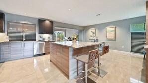 A modern kitchen with a large island, stainless steel appliances, and a bar area with stools. - Luxurious Naples Home. Heated Pool. Mins to Beach. (Naples)