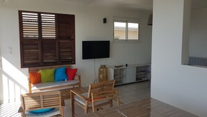 Una stanza con un divano in legno, una TV fissata al muro e un tavolino con sedie.