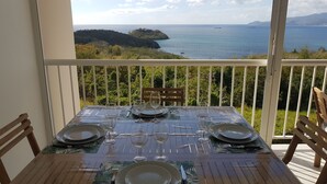 Tavola imbandita per quattro su un balcone con vista sul mare e una piccola isola.