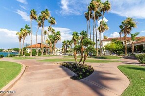 A well-maintained resort with a curved driveway, palm trees, and a building with a red-tiled roof. - Val Vista Oasis- Gorgeous Gilbert Home with Pool (Gilbert)