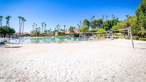 A beach volleyball court with a net, surrounded by palm trees and a clear blue sky. - Val Vista Oasis- Gorgeous Gilbert Home with Pool (Gilbert)