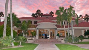 A large, multi-story building with a red-tiled roof, surrounded by palm trees and a well-maintained lawn. - Val Vista Oasis- Gorgeous Gilbert Home with Pool (Gilbert)