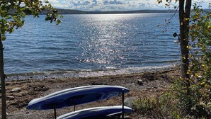 A lakeside view with a rocky shore, a boat, and trees. - Sunrise Lake House, Comfort-Hot Tub-Beach! (Saint Albans)