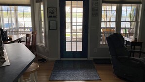 A room with a wooden floor, a blue door, a bar area with stools, and large windows offering a view of the outdoors. - Sunrise Lake House, Comfort-Hot Tub-Beach! (Saint Albans)