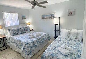 Ein Schlafzimmer mit zwei Betten, einem Deckenventilator, einem Fenster mit Jalousien und einem Bild an der Wand.