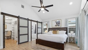 Une chambre dotée d’un grand lit, d’un ventilateur de plafond, d’un plancher en bois, d’un tapis moelleux et d’une porte coulissante donnant accès à un dressing.