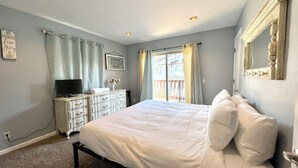 Ein Schlafzimmer mit Bett, Schminktisch, Fernseher und einem Fenster mit Vorhängen.