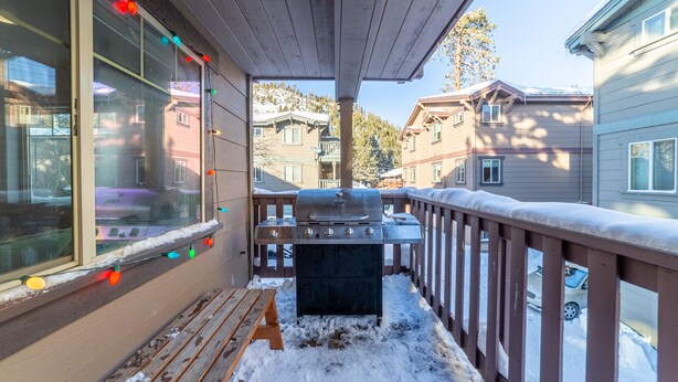 Eine überdachte Terrasse mit Grill, Holzgeländern und Blick auf angrenzende Häuser.