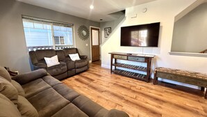 Ein Wohnzimmer mit einem Ecksofa, einem Couchtisch und einem an der Wand befestigten Fernseher.