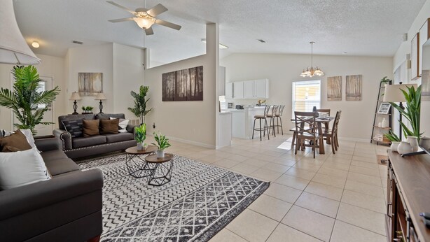 A spacious living room with a dark sofa, a patterned rug, and a ceiling fan.