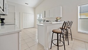 A modern kitchen with white cabinetry, a central island with stools, and a view of the adjacent dining area.