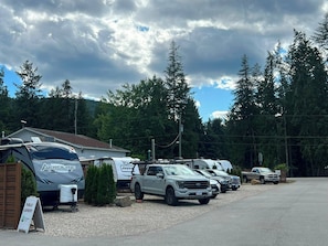 A campground with RVs and trucks parked, surrounded by trees and a cloudy sky.