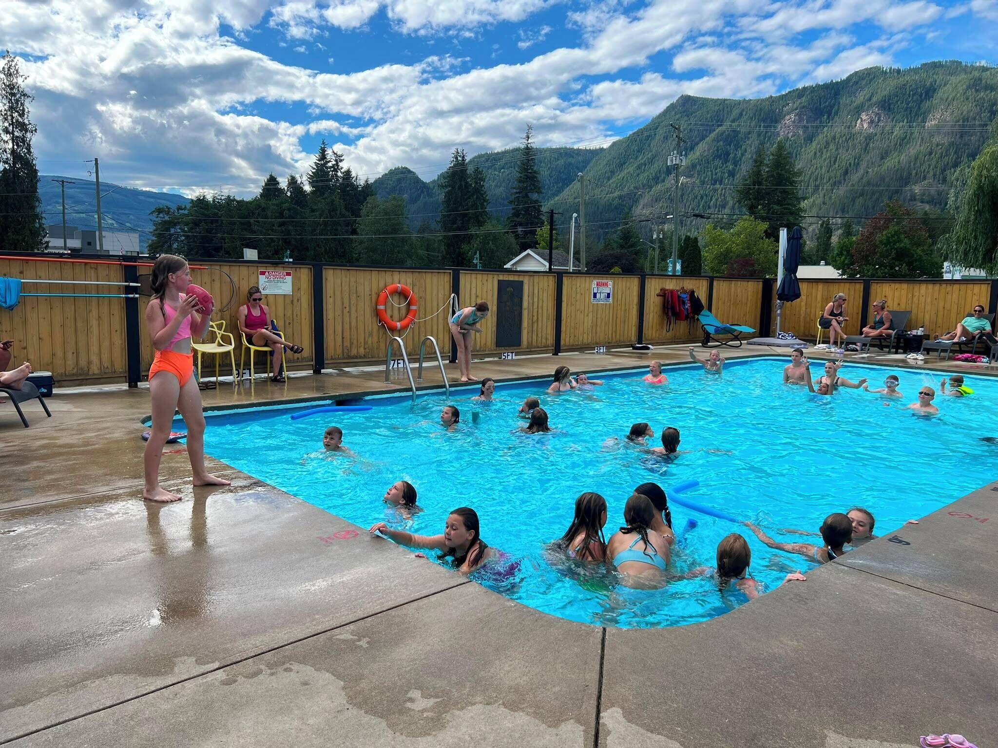 Une piscine entourée d’une clôture en bois, avec des montagnes en arrière-plan.