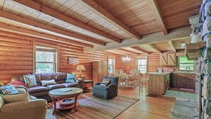 Interior de uma cabana de tronco com sala de estar, sala de jantar e cozinha.