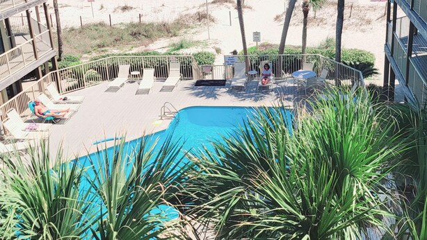 Ett poolområde med solstolar och utsikt över stranden och havet.