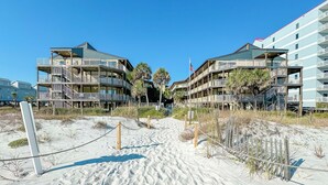 Ett hotell vid stranden med flera balkonger, en sandstig som leder till entrén och en amerikansk flagga.