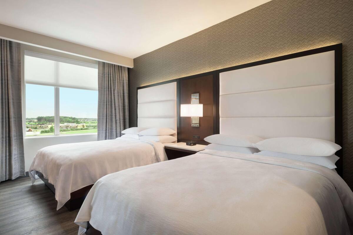 A hotel room with two beds, a large window, and a view of the countryside.
