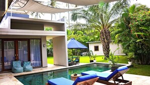 Une piscine avec des chaises longues, un patio couvert et un bâtiment moderne doté d’une porte en verre.