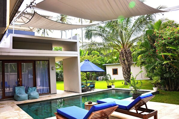 A swimming pool with lounge chairs, a covered patio, and a modern building with a glass door.