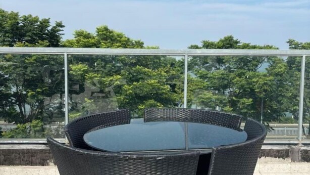 A round glass table with wicker chairs on a balcony with a glass railing, overlooking a garden with trees. - Shell Hotel (Suzhou Yangcheng Lake Peninsula Yangcheng Peninsula Park)‌ (Suzhou)