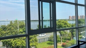 A view through large windows of a river, greenery, and distant buildings. - Shell Hotel (Suzhou Yangcheng Lake Peninsula Yangcheng Peninsula Park)‌ (Suzhou)