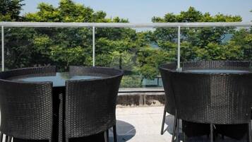An outdoor seating area with wicker tables and chairs, overlooking a view of trees and a clear sky.