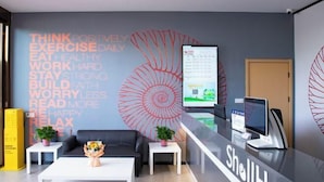 A modern reception area with a Shell logo, a large motivational poster, a reception desk, and a seating area with a sofa and coffee table. - Shell Hotel (Suzhou Yangcheng Lake Peninsula Yangcheng Peninsula Park)‌ (Suzhou)