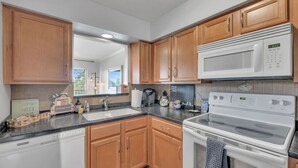 A kitchen with wooden cabinets, a microwave, a stove, a sink, and a window. - Nash Riverfront Condo, Sleeps 6, Walk to Broadway (Nashville)