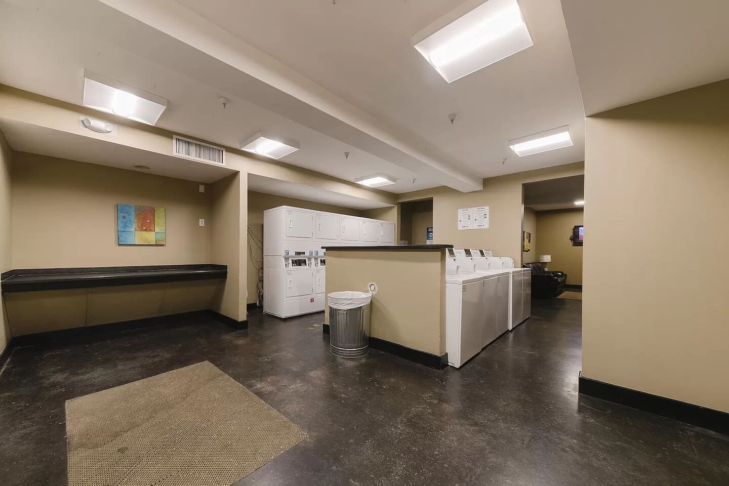 A laundry facility with washers and dryers, a trash can, and a wall-mounted sign.