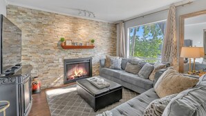 A living room with a stone wall, fireplace, grey sofa, and a large window. - Nash Riverfront Condo, Sleeps 6, Walk to Broadway (Nashville)